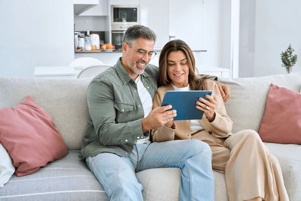 Happy couple browsing listings on a tablet and a homeowner preparing a home for sale.